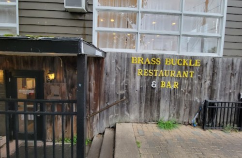 Entrance to the Brass Buckle Restaurant & Bar, featuring a wooden fence and a staircase leading up.