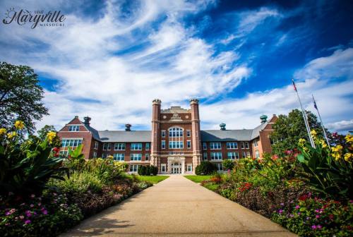 Historic building with a grand entrance, surrounded by colorful flowers and a bright blue sky.