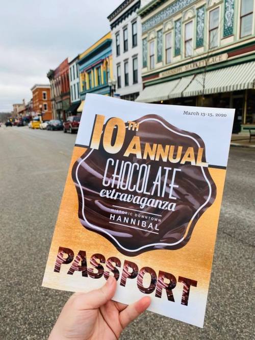 A person holds a flyer for the 10th Annual Chocolate Extravaganza in Hannibal, March 13-15, 2020, with a street view in the background.