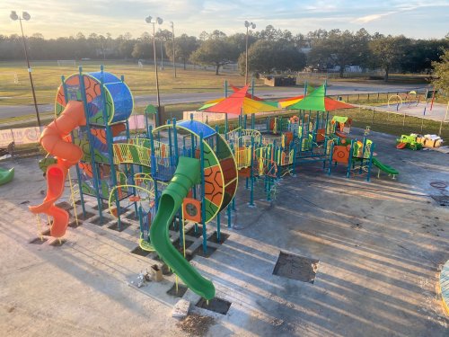 Colorful playground equipment with slides and climbing structures, set in a grassy area under a clear sky.