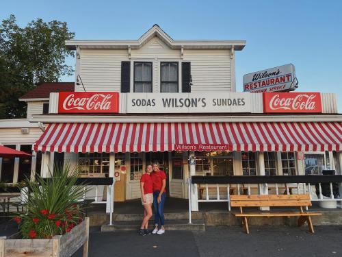 Two women in red shirts stand in front of Wilson's Restaurant, featuring a striped awning and Coca-Cola signage.