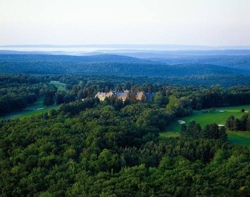 Aerial view of a lush green landscape with a large estate surrounded by trees and rolling hills in the background.