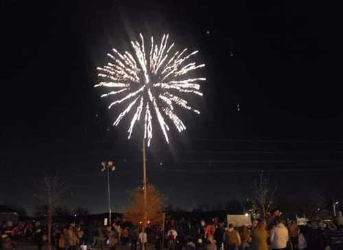 A crowd watches fireworks explode in the night sky, illuminating the dark with bright colors.