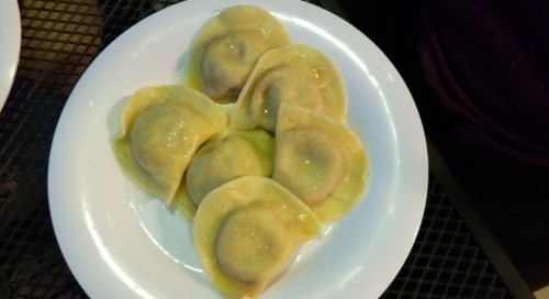 A white plate with six dumplings, lightly coated in a yellow sauce, arranged neatly.
