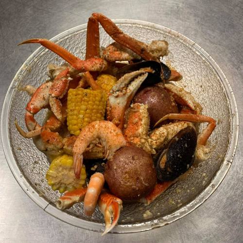 A bowl of seafood featuring crab, shrimp, mussels, corn, and potatoes, seasoned and ready to eat.