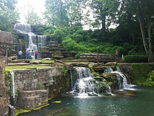 A scenic waterfall surrounded by lush greenery, with people enjoying the view near the water's edge.