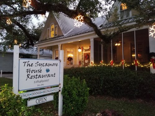 A charming restaurant with festive decorations, featuring a sign that reads "The Sycamore House Restaurant" and "Open."