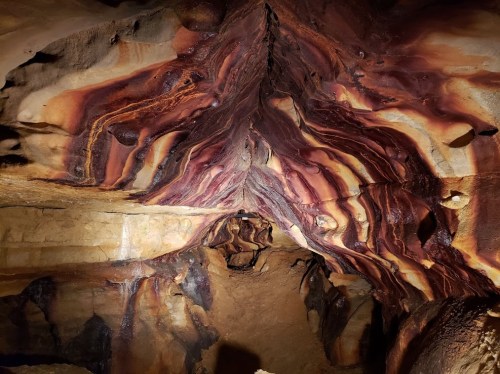 Colorful, swirling rock formations inside a cave, showcasing shades of red, orange, and brown.