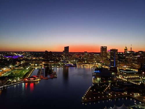 A vibrant city skyline at sunset, reflecting on the water with colorful lights and a clear sky.