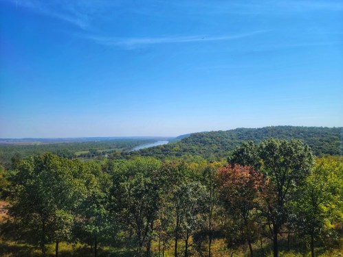 A scenic view of a river winding through lush green hills under a clear blue sky.