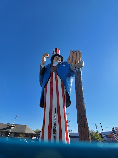 A large statue of Uncle Sam in a blue coat and red-striped pants, holding a cane against a clear blue sky.