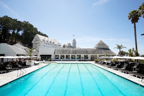 A sunny pool area with lounge chairs, surrounded by palm trees and a historic building in the background.