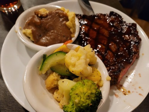 A plate with grilled steak, mashed potatoes with gravy, and a side of mixed vegetables including broccoli and cauliflower.