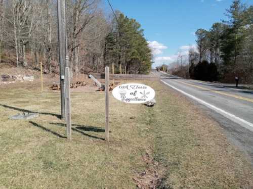 Sign for "A Taste of Excellence" along a rural road, surrounded by trees and grassy areas.