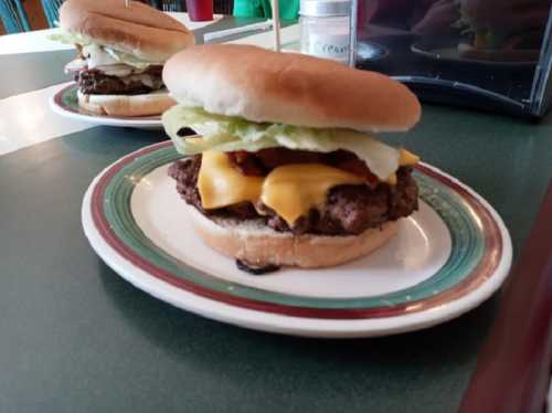 A close-up of a cheeseburger with lettuce and bacon on a plate, with another burger in the background.