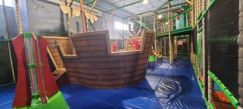 Indoor play area featuring a large wooden pirate ship and various climbing structures on a blue floor.