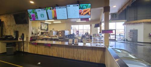 Interior view of a café with digital menus, a service counter, and large windows letting in natural light.