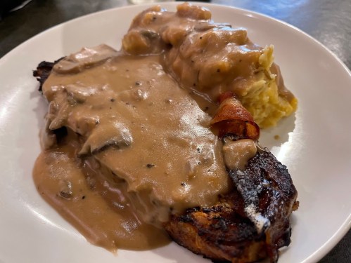 A plate featuring a grilled steak topped with creamy mushroom gravy, served alongside mashed potatoes.