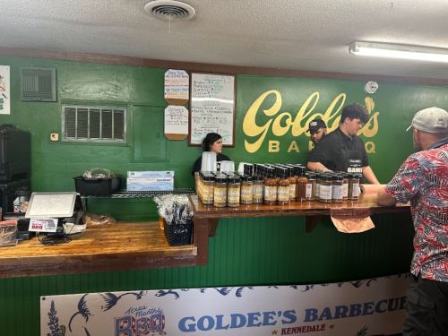 A busy barbecue restaurant counter with staff serving customers and various sauces displayed on the counter.