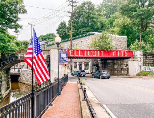 A street view of Ellicott City featuring a red sign, American flag, and historic buildings along a canal.