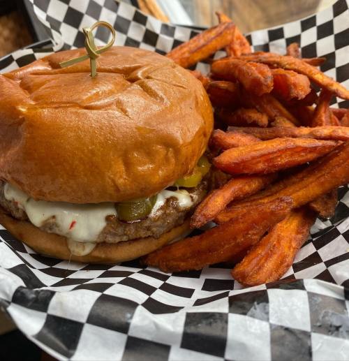 A juicy burger with pickles and melted cheese, served with crispy sweet potato fries in a checkered basket.