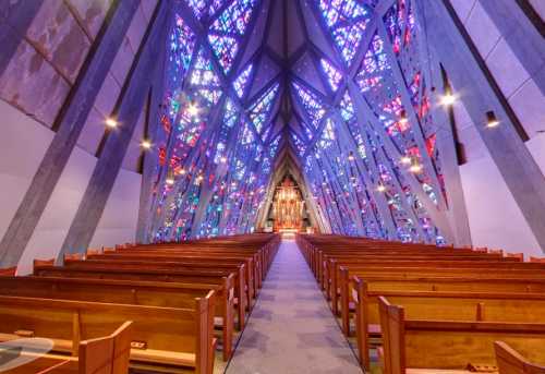 Interior of a modern church featuring colorful stained glass windows and wooden pews, creating a serene atmosphere.