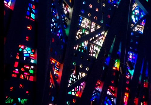 Colorful stained glass patterns illuminated through a dark, intricate framework, creating a vibrant, abstract design.