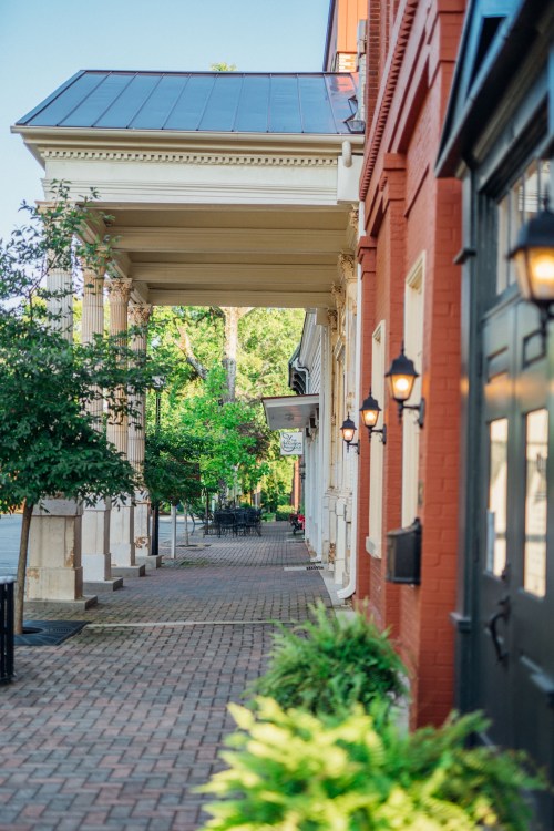 A charming street view featuring brick sidewalks, greenery, and historic buildings with decorative lighting.