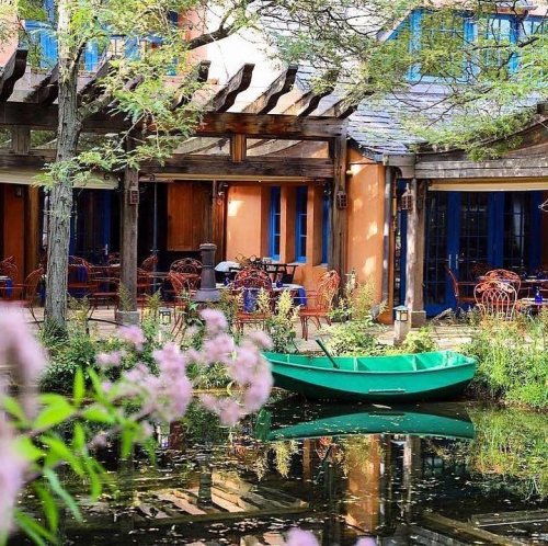 A serene outdoor scene featuring a green boat on a pond, surrounded by lush greenery and colorful seating areas.