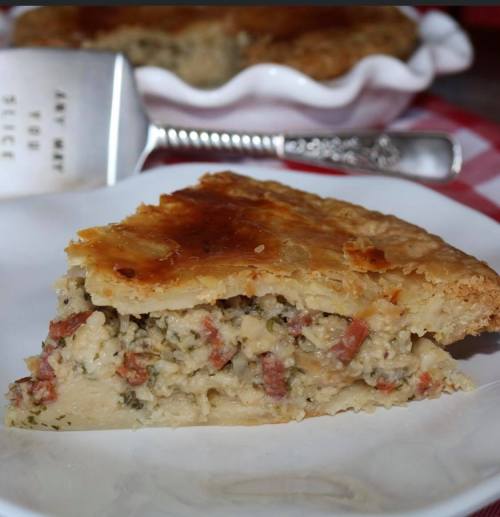 A slice of savory pie with a golden crust and filling of meat and herbs, served on a white plate.