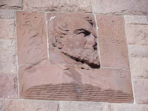 Relief sculpture of a bearded man on a stone wall, with inscriptions of his birth and death dates.