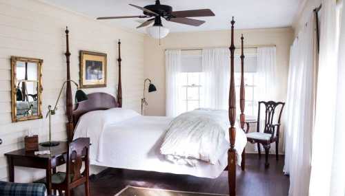 Bright bedroom with a four-poster bed, wooden furniture, and large windows letting in natural light.