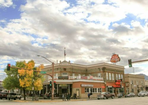 Historic building at a street corner with a bright sign, surrounded by trees and a cloudy sky.