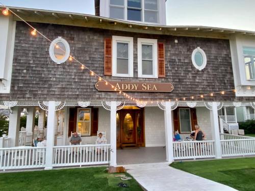 Exterior of the Addy Sea building, featuring a wooden facade, round windows, and string lights, with people seated outside.