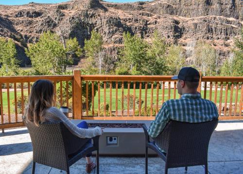 A couple sits on a patio, overlooking a scenic view of trees and rocky hills in the background.