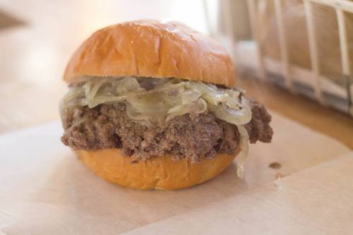 A close-up of a sandwich with a soft bun, filled with seasoned ground beef and topped with sautéed onions.