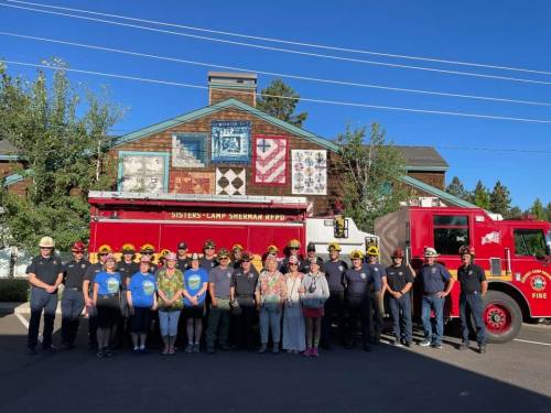 A group of firefighters and community members pose in front of a fire truck and a mural on a building.