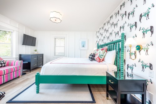 Brightly decorated bedroom featuring a green bed, patterned wallpaper, a TV, and colorful furnishings.