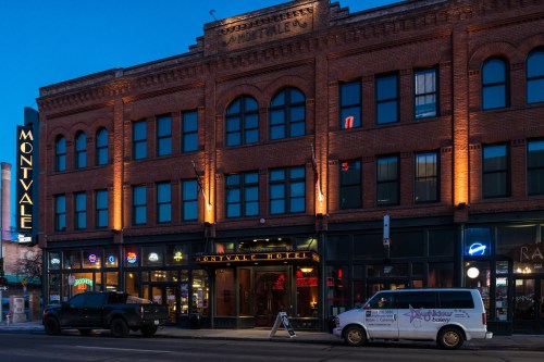 Historic brick building at dusk, featuring Montvale Hotel signage and illuminated storefronts.