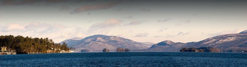 A panoramic view of a serene lake surrounded by mountains and trees under a clear sky.