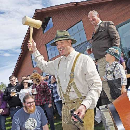 A man in traditional attire swings a large mallet, surrounded by a crowd enjoying a festive outdoor event.