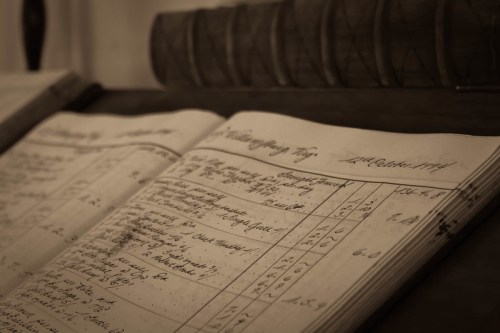 A close-up of an open ledger with handwritten entries, resting on a wooden surface.