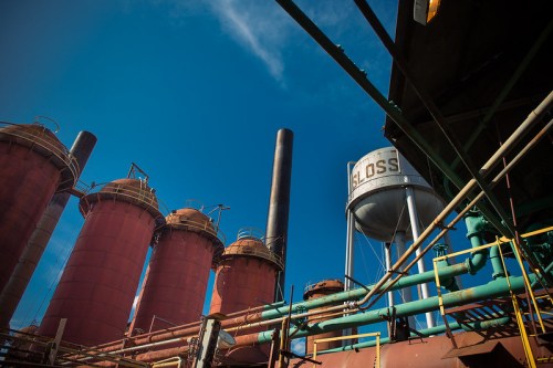Industrial scene featuring large red silos, a water tower, and pipes against a clear blue sky.