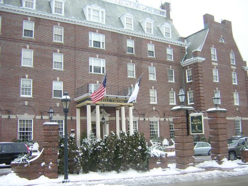 Historic brick hotel with flags, surrounded by snow and lampposts, featuring a welcoming entrance.