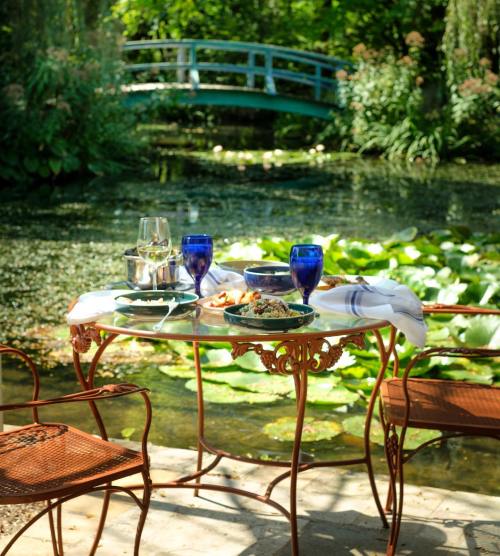A charming outdoor table set for a meal, overlooking a serene pond with lily pads and a blue bridge in the background.