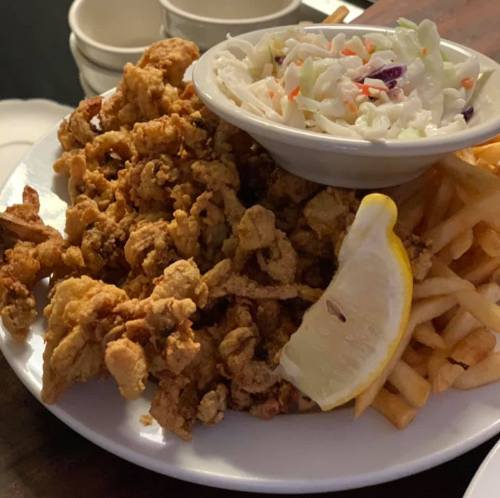 A plate of fried food featuring crispy fried chicken, coleslaw, French fries, and a lemon wedge.