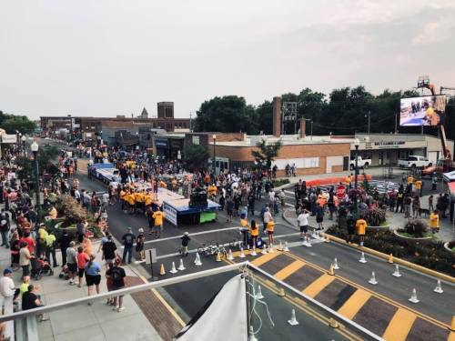 A bustling street scene during a parade, with crowds, floats, and participants in yellow shirts.