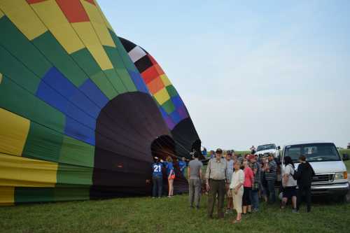 A colorful hot air balloon being prepared for launch, with a crowd of people gathered around it on a grassy field.