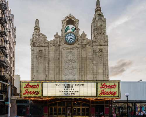 Historic theater facade with a clock, featuring a marquee that reads "Folks to India Benefit" and "Thank You."
