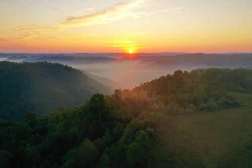 A serene sunrise over misty hills, with vibrant orange and yellow hues illuminating the landscape.